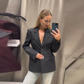 Elegant women's black suit jacket with slim lapel and single button closure, modeled in fitting room.