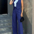 Women's blue blazer pant set with sleeveless notched waistcoat and high-waist straight pants, worn with a white top and black handbag.